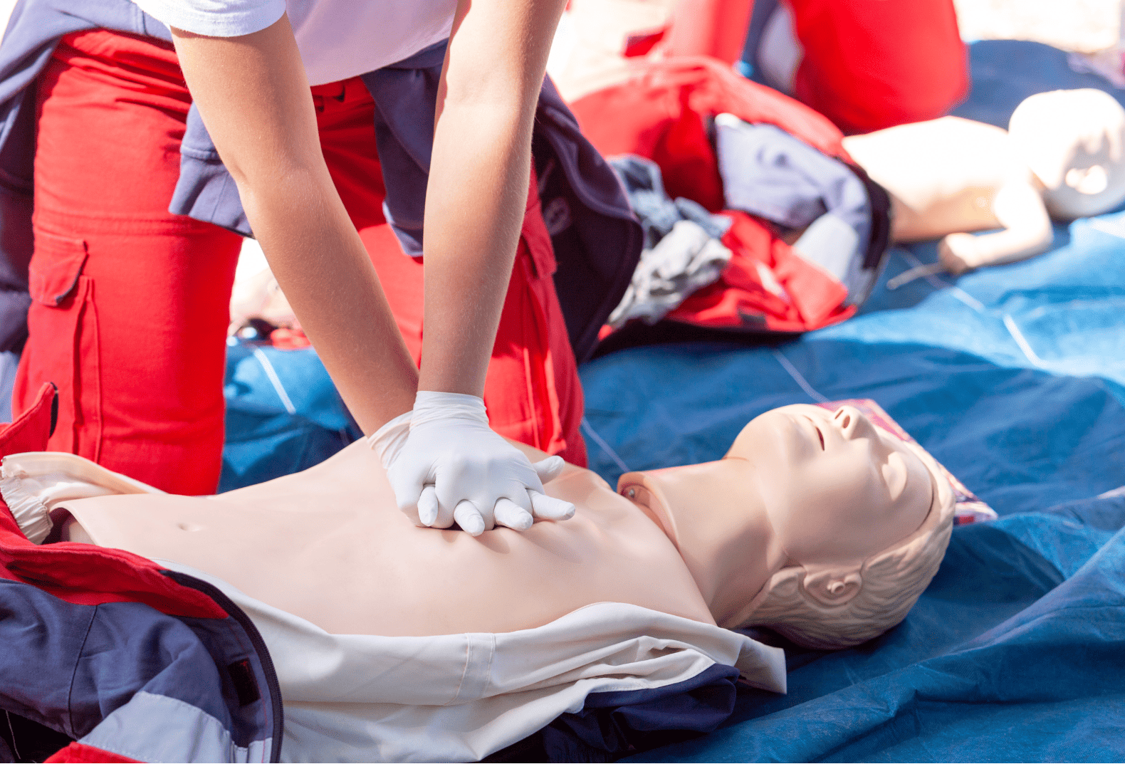 a person in a red shirt and white gloves is performing first aid on a mannequin 