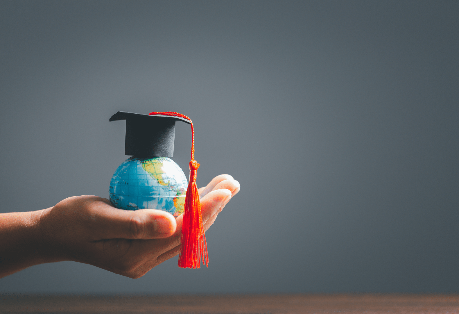 a hand holding a globe with a graduation cap on it