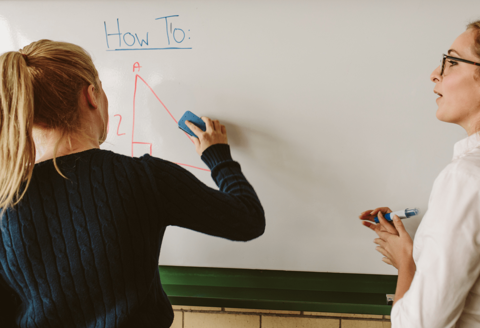 Two people standing in front of a whiteboard writing on it