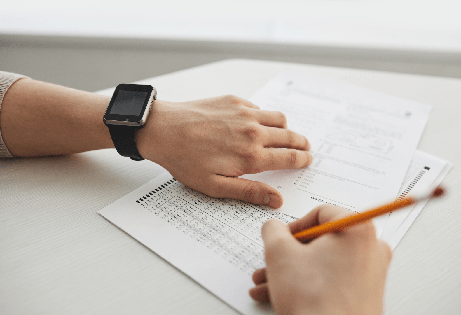 a person sitting at a desk with a pencil and a watch answering a test